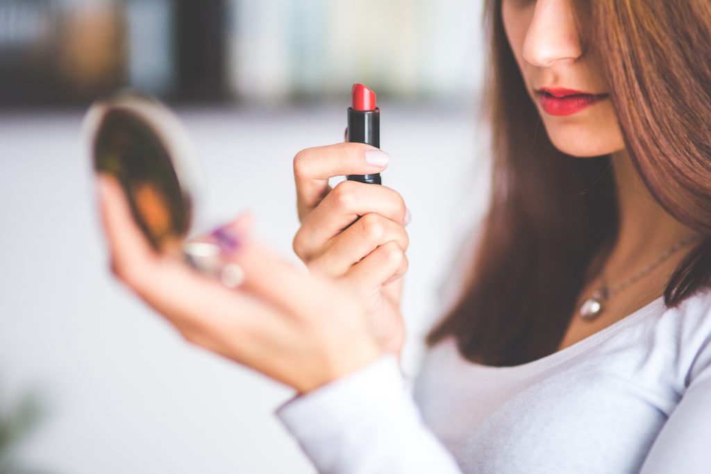 woman with compact applies red lipstick
