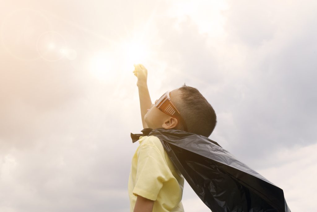boy with cape and glasses reaches for sun